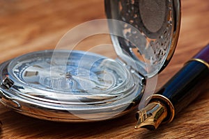 Fountain pen and pocket watch on a wooden table