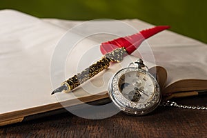 Fountain pen with red feather, an old watch and a notebook with green background, selective focus