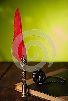 Fountain pen with red feather, an old watch and a notebook with green background, selective focus