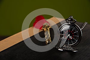 Fountain pen with red feather, an old watch and a notebook with green background, selective focus