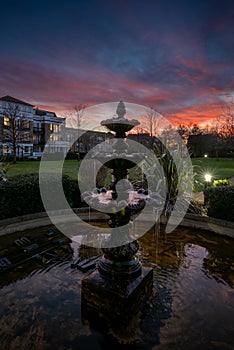Fountain and pond in a park at sunset with a pink sky