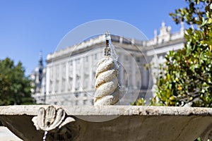 Fountain. Stone fountain filled with water. In the background the Royal Palace is out of focus. In a park in Madrid on a clear day