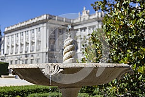 Fountain. Stone fountain filled with water. In the background the Royal Palace is out of focus. In a park in Madrid on a clear day