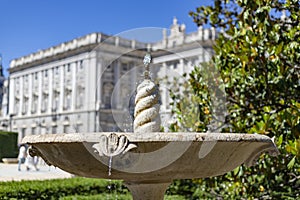 Fountain. Stone fountain filled with water. In the background the Royal Palace is out of focus. In a park in Madrid on a clear day