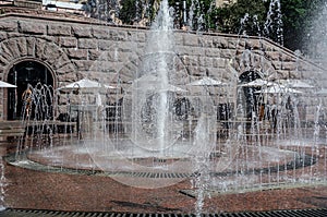 Fountain on the street, water splashes play in the sun. Summer sunny day.