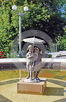 The fountain in the Strukovsky garden with the established bronze sculpture of the boy and girl under an umbrella in the sunny day