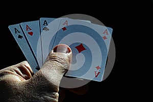 Four aces from canasta joker from French deck held in male left hand on dark background