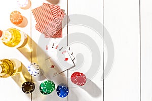 Four aces surrounded by poker chips and beer on white wooden background and copy space