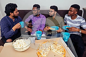 Four african american males eating pizza at home party,throwing popcorn into each other