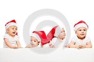 Four babies stand in a row wear red Christmas hats