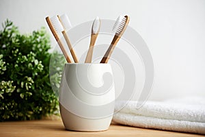 Four bamboo toothbrushes in a glass on a wooden background