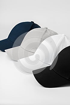 Four Baseball Caps in Black, White, Grey, and Blue Arranged on a Plain Background