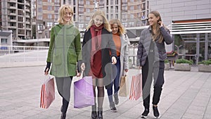 Four beautiful girlfriends walking on the street talking happily. Four fashion women with shopping bags walking in the