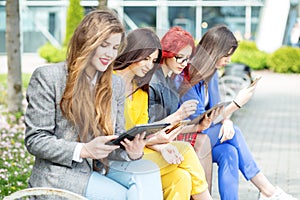 Four beautiful girls with gadgets are sitting on the bench. The concept of the Internet, social networks, study and lifestyle