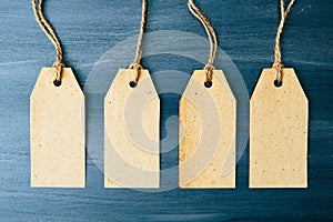 Four blank cardboard labels over brown wooden background. Four paper blank tags with rope on wooden background