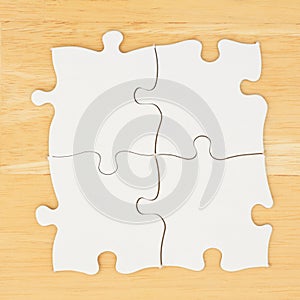Four blank puzzle pieces on textured desk wood background