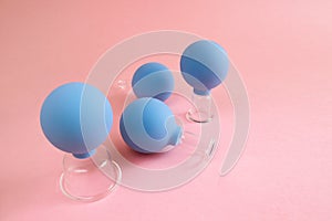 Four blue cosmetic vacuum jars for body and face massage of different sizes made of glass and rubber on pink background.