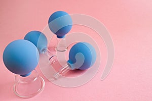 Four blue cosmetic vacuum jars for body and face massage of different sizes made of glass and rubber on pink background