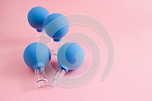 Four blue cosmetic vacuum jars of different sizes made of glass and rubber on pink background