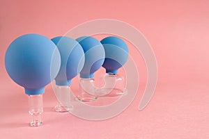 Four blue cosmetic vacuum jars of different sizes made of glass and rubber on pink background