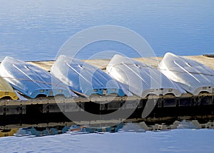 Four boats lined up on in storage a pier in a blue lake.