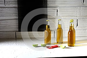 Four bottles of cold beer with slices of lime and a bottle opener on a white table