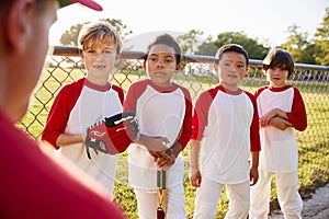 Four boys in a baseball team listening to coach, close up