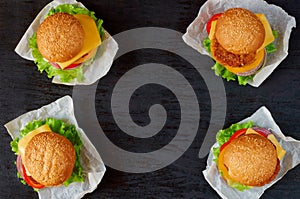 Four burgers with falafel, salad, onion rings, cheese and tomatoes on the black background. Classic american veggie fast food