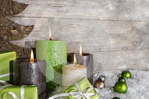 Four burning advent candles in green and brown on wooden background.