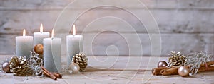 Four burning candles and Christmas decoration like cones, cinnamon and baubles against a rustic wooden background in pastel