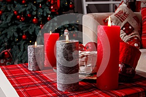 Four burning candles on a table close-up in front of a Christmas tree, selective focus. Christmas setting, selective focus.