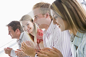 Four business people applauding indoors smiling