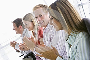 Four business people applauding indoors smiling