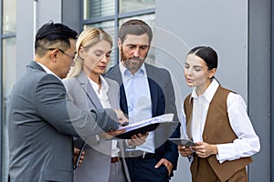 Four business people discussing financial results of achievement, mature men and women outside office building