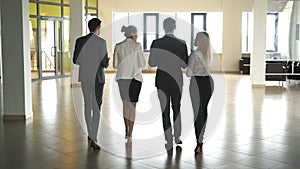 Four business people talking and walking in office lobby