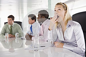 Four businesspeople in boardroom with one yawning