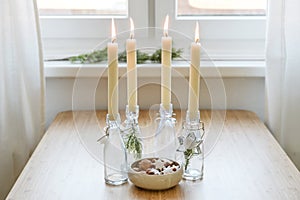 Four candles in bottles is lit for Advent, Christmas cookies and decoration on a table near the window, copy space, selected focus