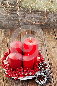 Four candles in a white wreath with red berries on a wooden rustic background with lights. advent calendar for Christmas