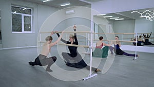 Four Caucasian slim graceful women doing tendu plie ballet movement at barre rehearsing in dance studio indoors