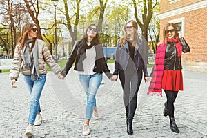 Four cheerful and beautiful women walk, holding hands, on the spring city in sunglasses. The concept of female