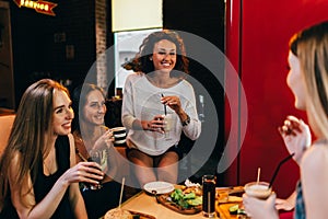 Four cheerful girlfriends having fun chatting and laughing eating and drinking in fast food restaurant