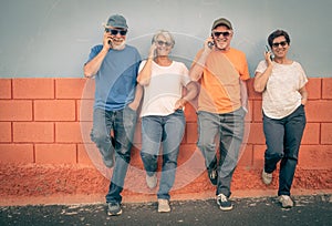 Four cheerful senior people standing outdoor using mobile phone. Four elderly enjoying retirement and fun