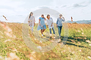 Four cheerful smiling women friends walking by a high green grass meadow. They looking at the camera. Woman\'s friendship,