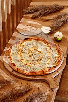 Four cheeses pizza with pear and honey on a traditional wooden plate. Wooden background, top view. Pizza Quattro formaggi