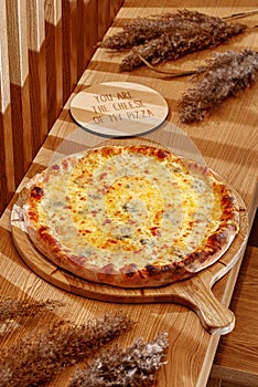 Four cheeses pizza on a traditional wooden plate. Wooden background, top view. Pizza Quattro formaggi