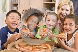 Four children indoors with woman eating pizza photo