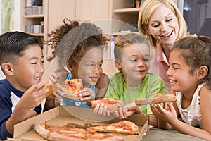 Four children indoors with woman eating pizza