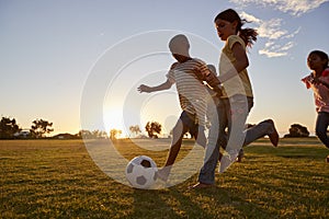 Four children racing after a football plying on a field