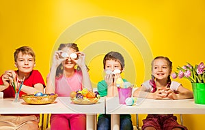 Four children sit at the table with Easter eggs