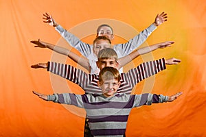 Four children stand in a row and raise their hands to the sides on the age of a yellow background, the younger ones look out for